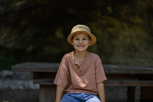 Portrait of happy boy sitting on bench and looking at camera in nature