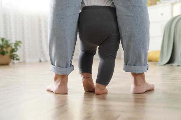istock Mother supporting her baby daughter while she learning to walk at home, closeup 1445191880