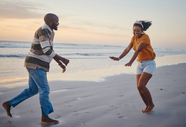 Love, freedom and couple at a beach at sunset, laughing and having fun on summer vacation in nature. Relax, sea and black woman and man being playful and joking, enjoying sand and ocean walk together amor, libertad y pareja en una playa al atardecer, riendo y divirtiéndose en las vacaciones de verano en la naturaleza. relájate, mar y mujer negra y hombre siendo juguetones y bromeando, disfrutando de la arena y el océano caminar juntos