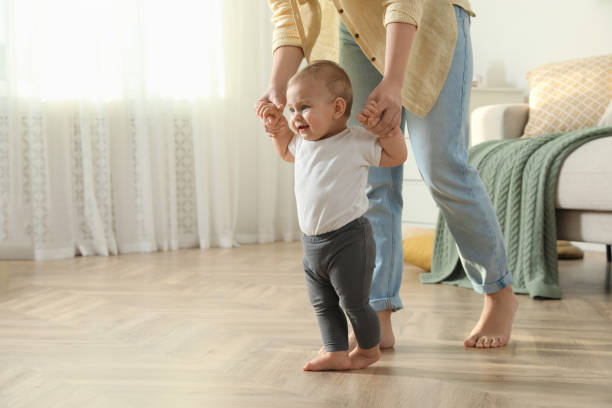 istock Mother supporting her baby daughter while she learning to walk at home 1445192929