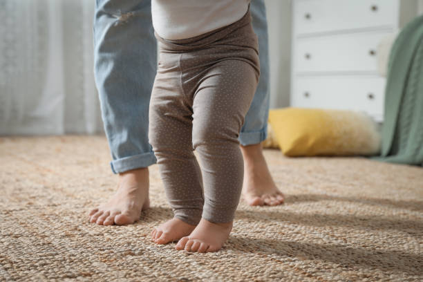 istock Mother supporting her baby daughter while she learning to walk at home, closeup 1445192949