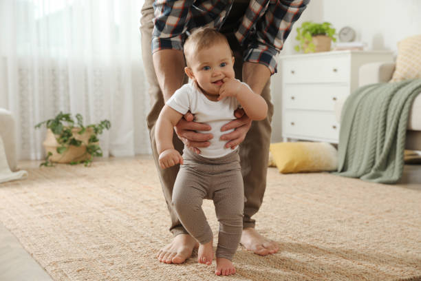 istock Father supporting his baby daughter while she learning to walk at home 1445193008