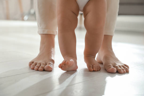istock Mother supporting her baby daughter while she learning to walk at home, closeup 1445193080