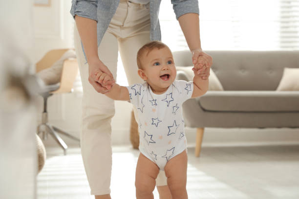 istock Mother supporting her baby daughter while she learning to walk at home 1445193081