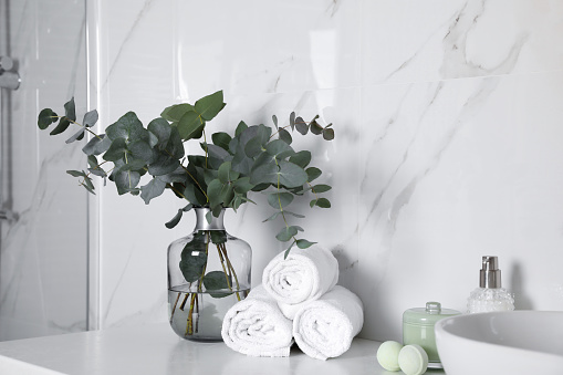 Towels, toiletries and glass vase with beautiful eucalyptus branches on bathroom counter. Interior design