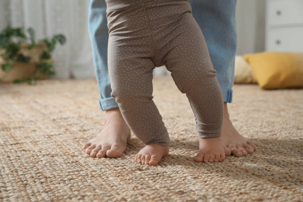 istock Mother supporting her baby daughter while she learning to walk at home, closeup 1445193507