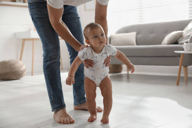 istock Father supporting his baby daughter while she learning to walk at home 1445193518