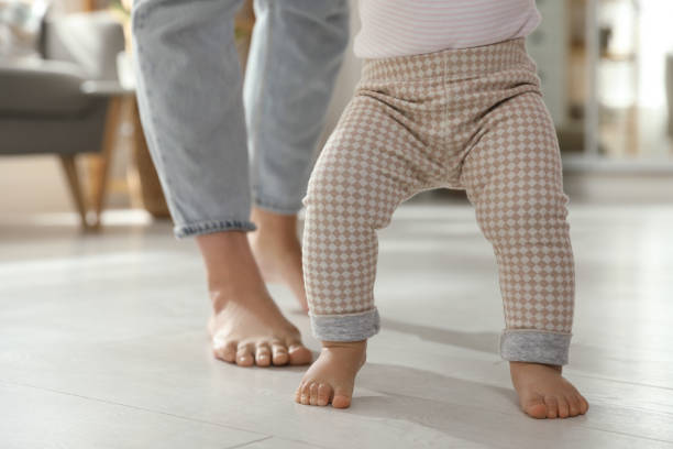 istock Mother supporting her baby daughter while she learning to walk at home, closeup 1445193519