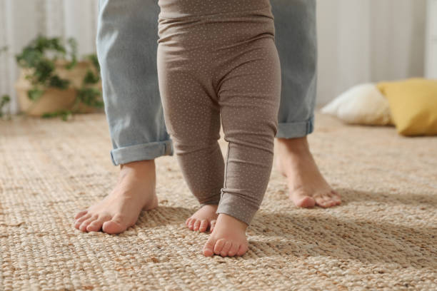 istock Mother supporting her baby daughter while she learning to walk at home, closeup 1445193590