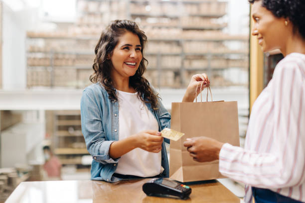 happy female customer paying with a credit card in a ceramic store - mercadoria imagens e fotografias de stock