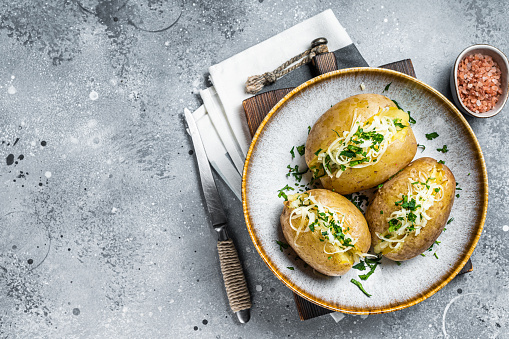 Baked Jacket potatoes with cheese and butter. Gray background. Top view. Copy space.
