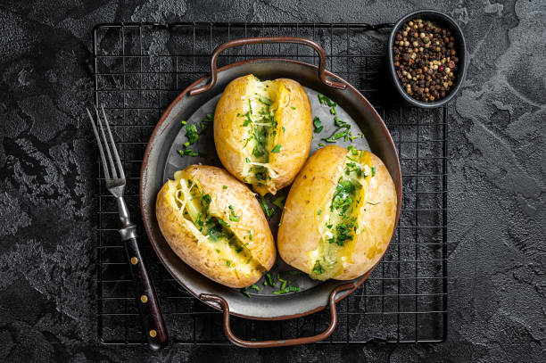 istock Baked Jacket potatoes with cheese, herbs and butter. Black background. Top view 1445196872
