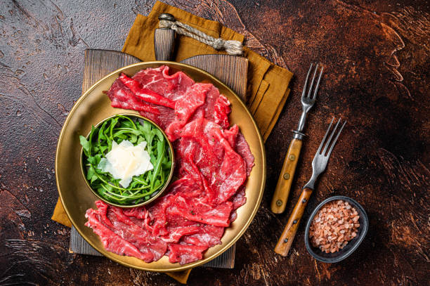 Carpaccio Beef meat appetizer with parmesan and arugula. Dark background. Top view Carpaccio Beef meat appetizer with parmesan and arugula. Dark background. Top view. carpaccio parmesan cheese beef raw stock pictures, royalty-free photos & images