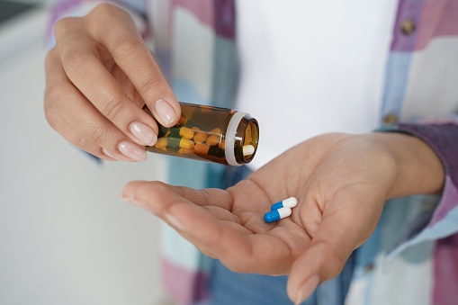 Female holding pills taking dietary supplements, vitamins or medicines, close up. Woman's hands pours medical capsules out of jar into palm to take painkiller or sleeping tablets for treatment.
