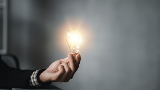 Standing man hold glowing light bulb, Creative new idea. Innovation, brainstorming, strategizing to make the business grow and be profitable. Concept execution, strategy planning and profit management