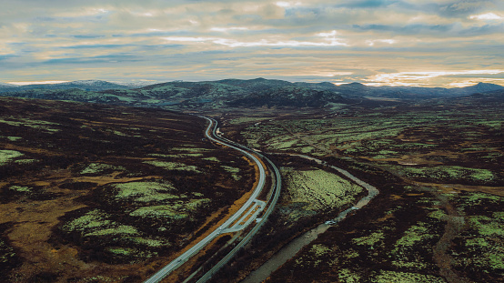 Drone photo of cars driving on the hairpin road trough the mountain tundra with view of the peaks in central Norway