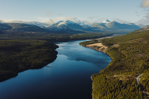 Drone high-angle photo the mountain pass with majestic view of the pine wooldand, reflection lake and the snowcapped mpuntain peaks in Scandinavia