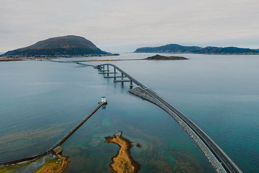 Drone photo of the vehicle on the modern bridge above the Norwegian Sea surrounded by the white lighthouse and the islands in More og Romsdal, Scandinavia