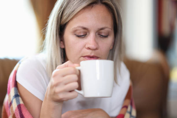 istock Woman sitting on sofa wrapped in blanket and drinking tea 1445199436