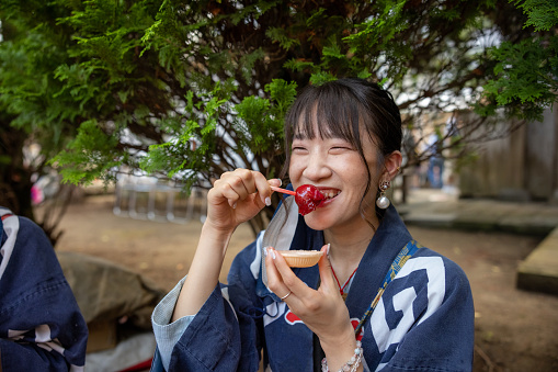 Young woman in traditional Japanese matsuri clothing eating apricot candy on street