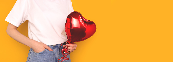 Banner with unrecognizable person hold in hands red inflatable foil balloon in a heart shape.