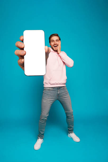 istock Handsome Excited Man Showing Pointing At Empty Smartphone Screen Posing Over Light Blue Background, Smiling To Camera 1445202149