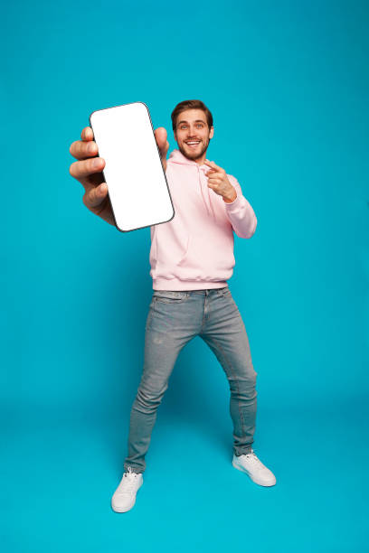 istock Handsome Excited Man Showing Pointing At Empty Smartphone Screen Posing Over Light Blue Background, Smiling To Camera 1445202150