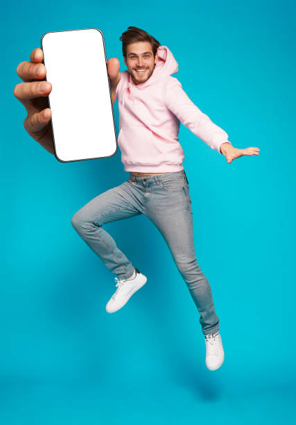 istock Handsome Excited Man Showing Pointing At Empty Smartphone Screen Posing Over Light Blue Background, Smiling To Camera 1445202154