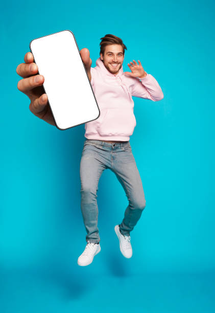 istock Handsome Excited Man Showing Pointing At Empty Smartphone Screen Posing Over Light Blue Background, Smiling To Camera 1445202155