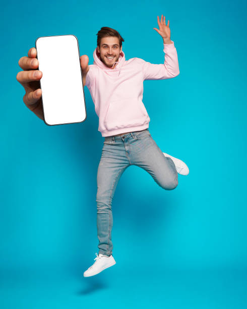 istock Handsome Excited Man Showing Pointing At Empty Smartphone Screen Posing Over Light Blue Background, Smiling To Camera 1445202157