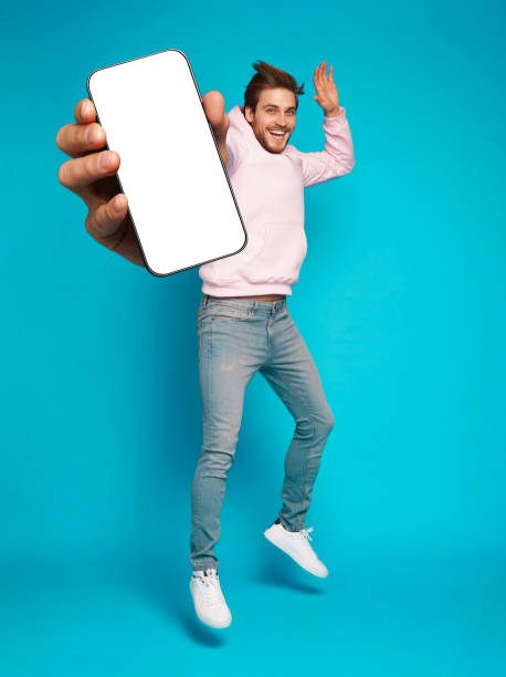 istock Handsome Excited Man Showing Pointing At Empty Smartphone Screen Posing Over Light Blue Background, Smiling To Camera 1445202159
