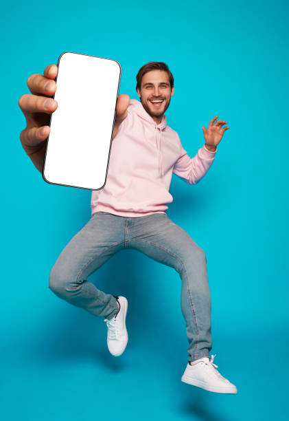 istock Handsome Excited Man Showing Pointing At Empty Smartphone Screen Posing Over Light Blue Background, Smiling To Camera 1445202188