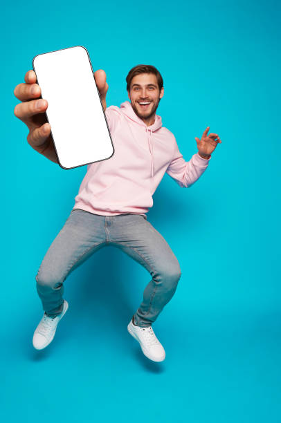 istock Handsome Excited Man Showing Pointing At Empty Smartphone Screen Posing Over Light Blue Background, Smiling To Camera 1445202189
