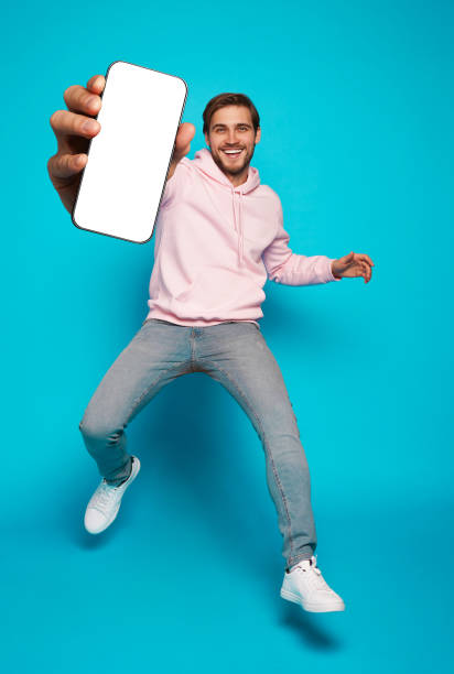istock Handsome Excited Man Showing Pointing At Empty Smartphone Screen Posing Over Light Blue Background, Smiling To Camera 1445202193