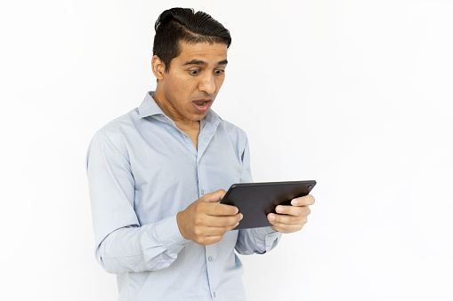 Shocked man holding tablet with both hands. Indian man in blue shirt with tablet expressing surprise. Portrait, studio shot, technology, surprise concept