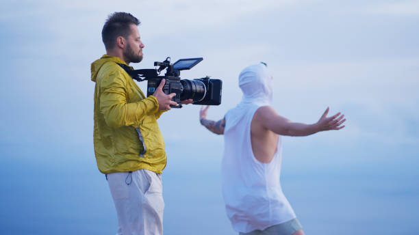 Filming a movie on windy day. Camera operator recording a man on a cliff