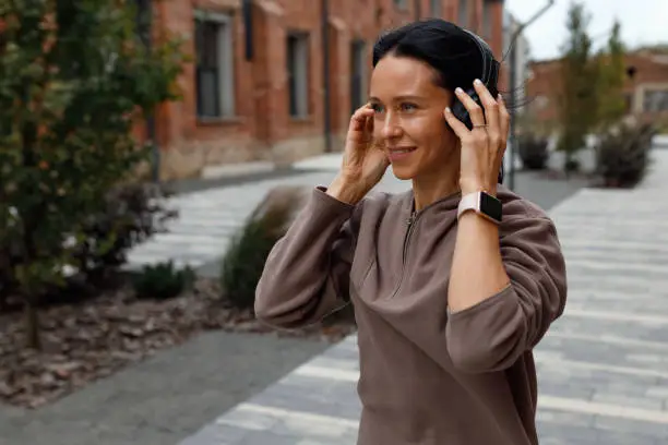 Photo of Portrait of adult athletic woman wearing headphones and listening to music outdoors