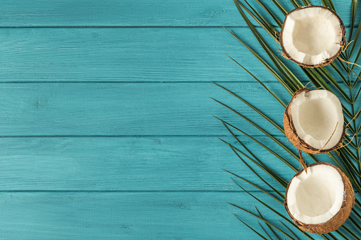 Coconut pieces with green palm leaves. Tropical fruit on the wooden turquoise background. Flat lay