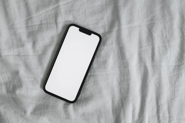 istock Smart mobile phone with blank mockup screen on wrinkled bed linen 1445205891