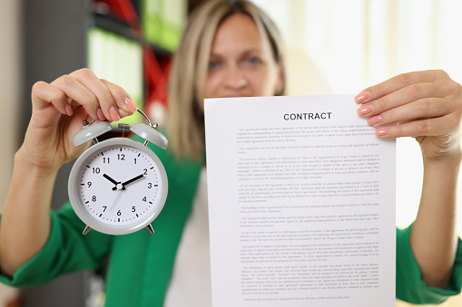 Close-up of businesswoman holding contract agreement and alarm clock. Signing and concluding business contracts