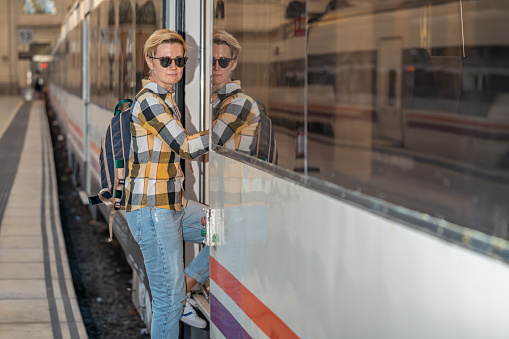 Adult 35s year old lesbian woman in plain shirt and jeans with backpack and sunglasses traveling by train in Europe. Train station in Barcelona, Spain.