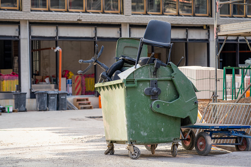 A large plastic industrial bin full of discarded office chairs at a building construction site.