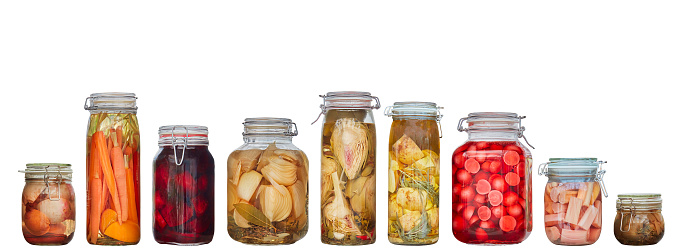 Row of nine glass canning jars with preserved vegetables isolated on a white background