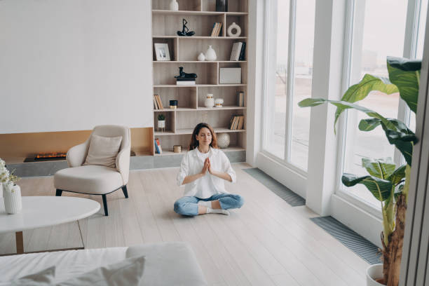 les femmes méditent en pratiquant le yoga assises par terre, respirant de l’air frais dans le salon moderne à la maison - floor women sitting yoga photos et images de collection