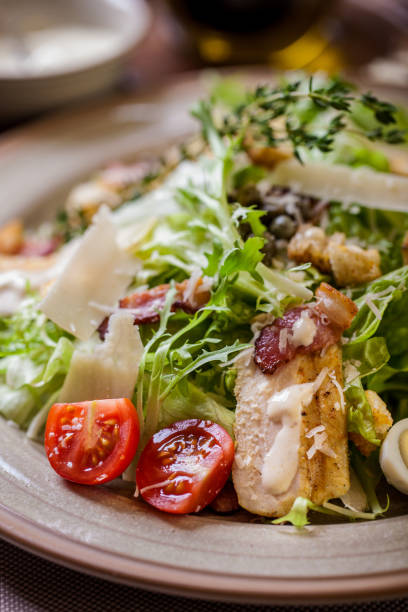 istock Salad with meat, tomatoes, lettuce, croutons, thyme, endive, boiled egg and mayonase in a plate on a light background with a glass of wine with cutlery 1445209531