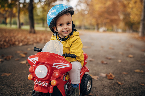 One boy, little boy sitting on his toy motorcycle on autumn day in park.