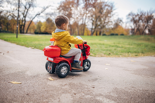 One boy, little boy ridding his toy motorcycle on autumn day in park.