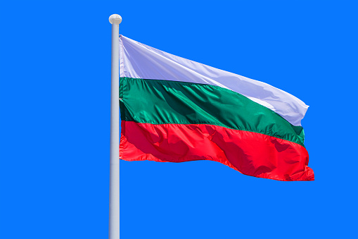 Bulgaria flag waving against clean blue sky, close up. Bulgaria flag in the blue sky. Flag Bulgaria on blue sky background