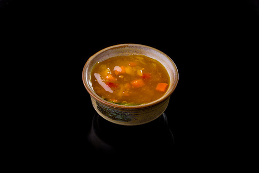 Mango and chili sauce in a ceramic, round, beige saucepan. A sauce-boat stands on a black, glossy background, reflected from below.