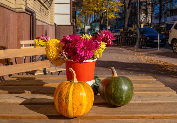 Bouquet of flowers and small pumpkins close-up on a wooden table outdoors on a sunny day stock photo